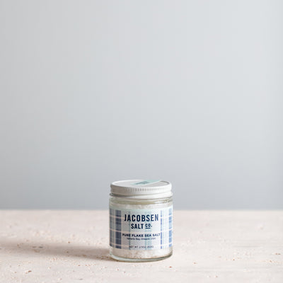 A glass jar of Jacobsen Pure Flake Sea Salt on a neutral background.