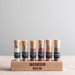 Six vials of Jacobsen pure and infused sea salts, including Flake, Black Pepper, Black Garlic, Pinot Noir, Habanero and Rosemary in a wooden branded stand