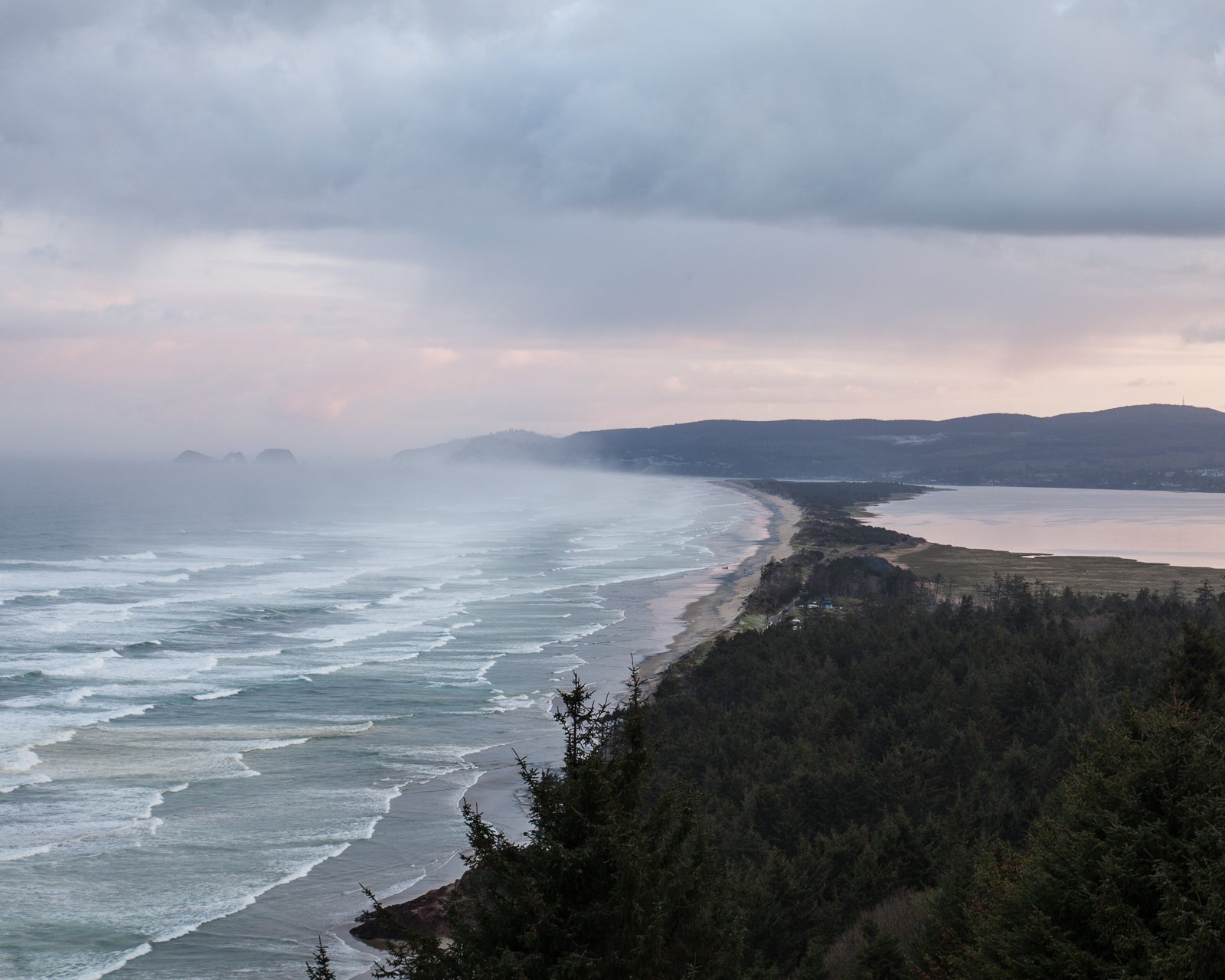 Rolling sea water coming in to meet Netarts bay under a cloudy grey sky. 