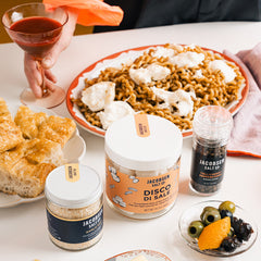 Jars of garlic salt and Disco di Sale with Tellicherry Pepperocorn grinder, on a set table with butter, a ramekin of olives, bread and pasta.