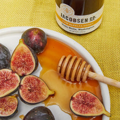 A jar of Jacobsen Raw Alfalfa Honey with a plate of dates on a light green picnic blanket