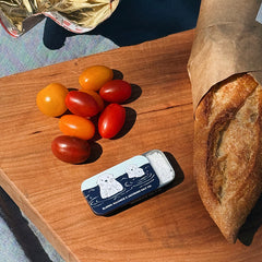 Tomatoes, a loaf of bread, and a sea otter slide tin filled with kosher salt on a wooden cutting board.