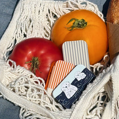 Tomatoes and a striped spatula in a mesh bag with a small box featuring a sea otter design.