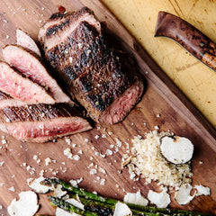 Cooked and sliced steak on a cutting board with asparagus, topped with flake salt.